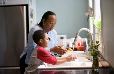 Grandmother and grandchild washing hands together in a kitchen